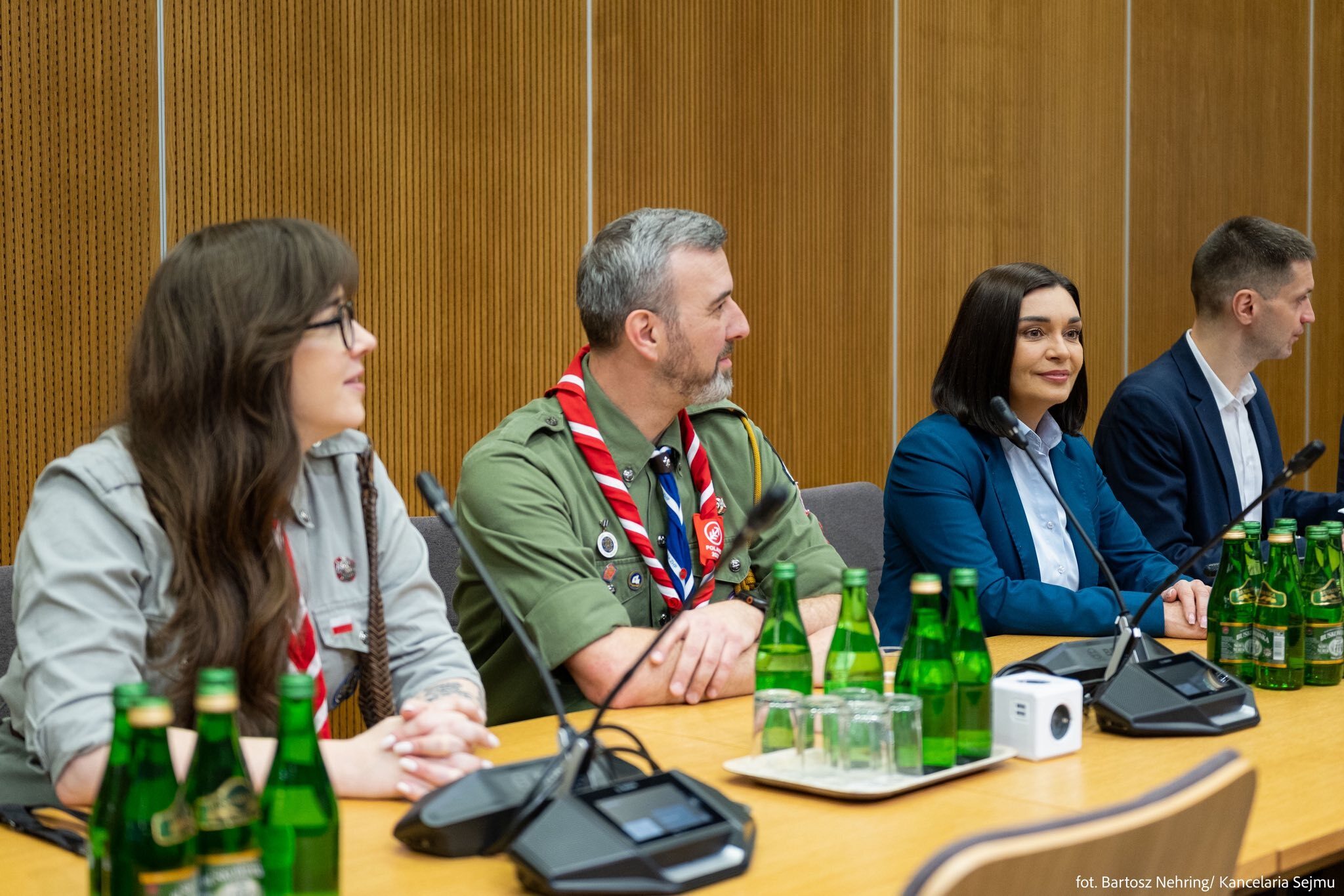 Members of the 26th World Scout Jamboree organizing team seated at a conference table during a meeting at the Polish Parliament. A scout leader in uniform with a red and white neckerchief is visible among the attendees.